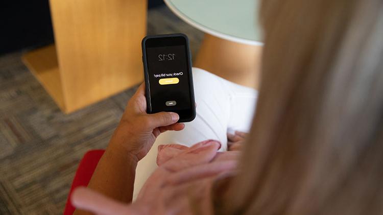 Woman sits looking at her mobile phone deciding if she should enroll in AutoPay.