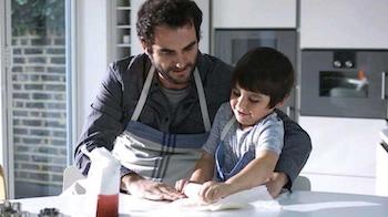 A dad helps his son as they roll out some dough